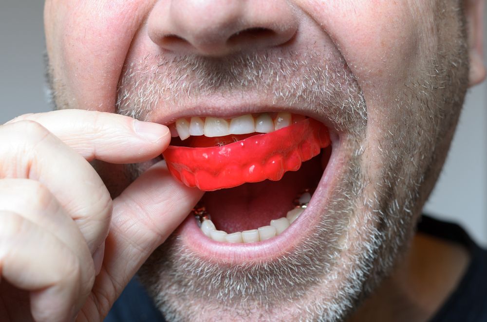 man placing red bite plate on mouth to protect teeth