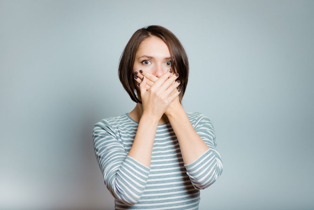 woman with bad breath holding her mouth​​​​​​​