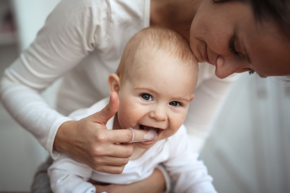Mom helps to brush the teeth of a happy baby