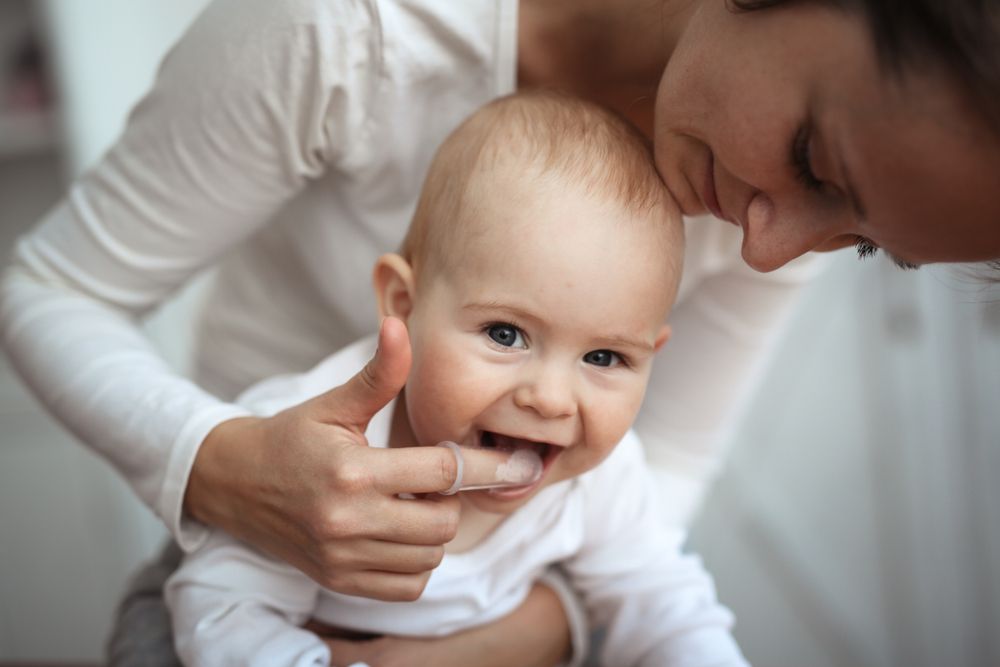 Mom helps to brush the teeth of a happy baby​​​​​​​