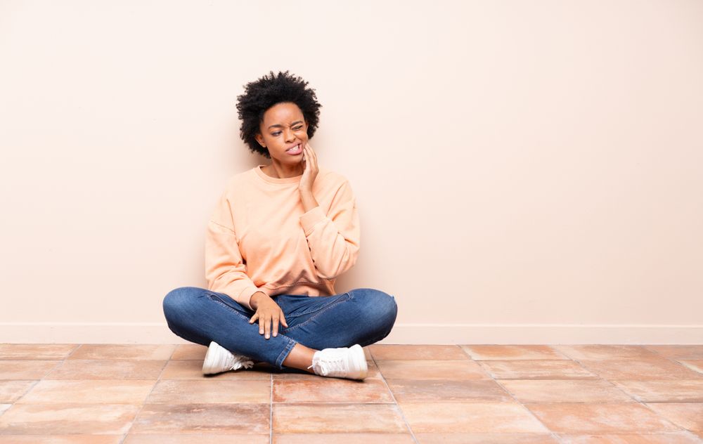 woman sitting on the floor holding her jaw, tmj pain