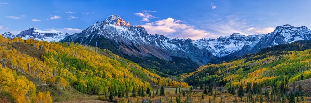 The last light of the setting sun hits the crags atop Mount Sneffels, with a mostly golden grove of quaking aspens below, in the San Juan Mountains near Ridgway, Colorado.