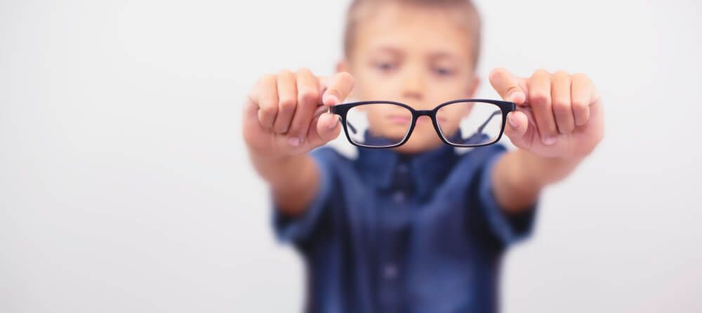 Young boy with myopia holding glasses