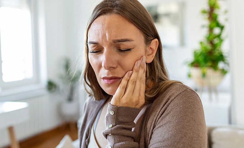 woman holding her jaw in pain, TMJ