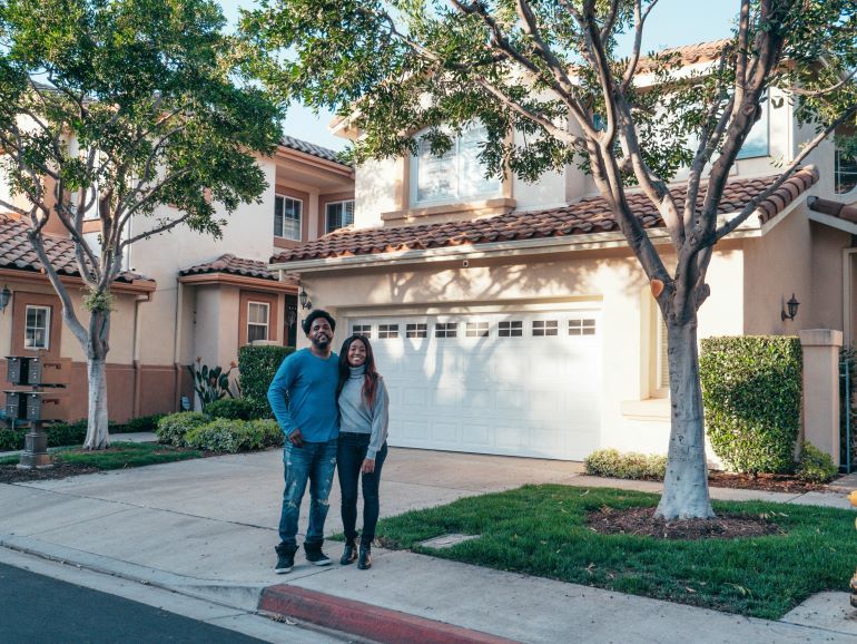 Couple standing together outside their home in an HOA neighborhood with landscaped trees and clean surroundings.