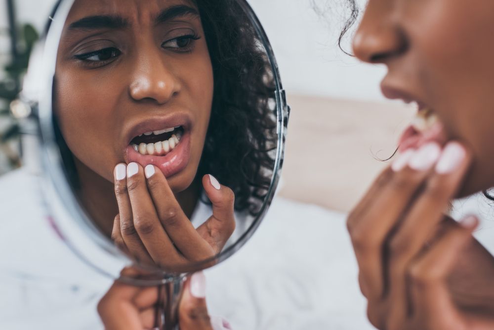 woman holding her mouth while looking in the mirror, toothache