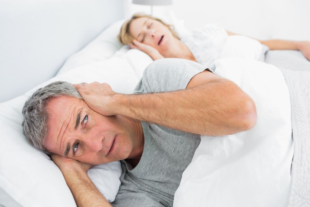 man trying to cover his ears from a snoring woman