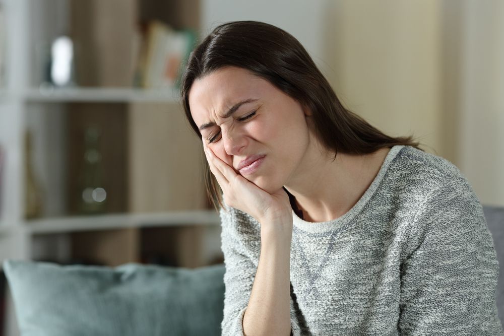 woman holding her jaw in pain, TMJ