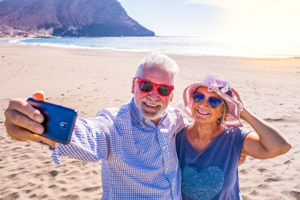 two retired seniors wearing sunglasses taking a selfie smiling