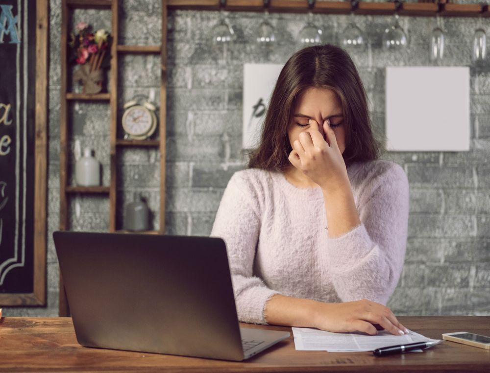 Woman rubbing her eye infront of her laptop