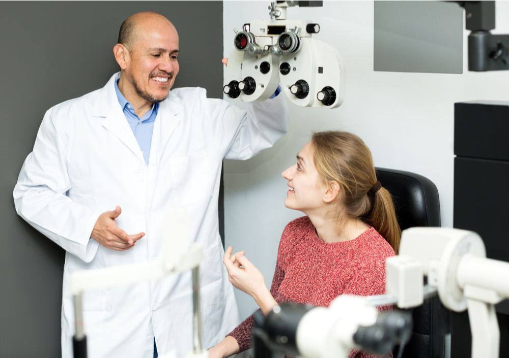 male optician doing an eye check up to smiling girl