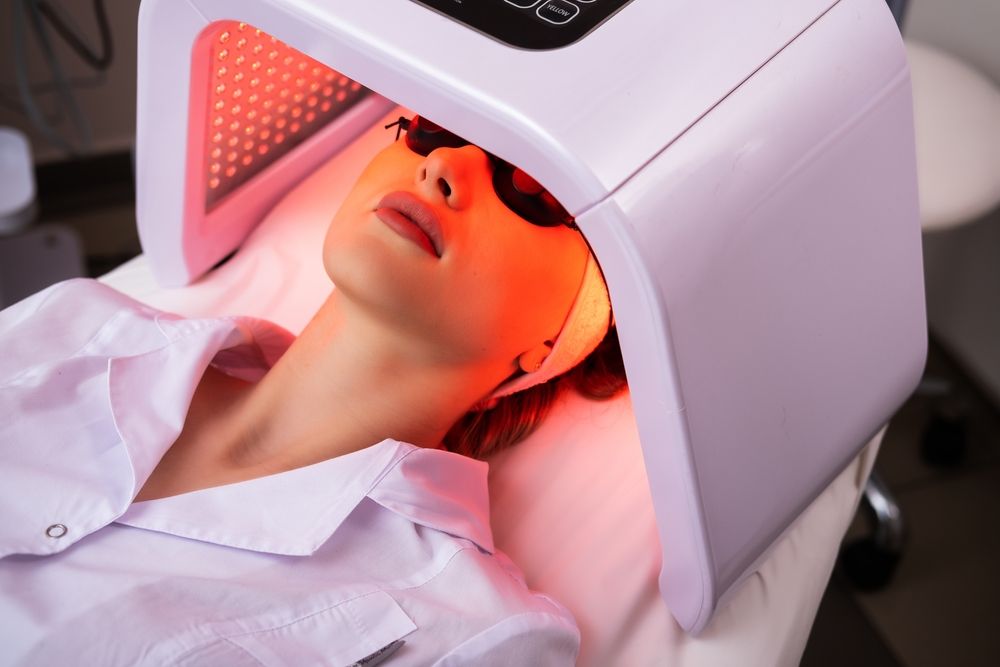 Express facial treatment with led therapy. Beautiful girl on a light therapy procedure. LED lamp with red light. Safe skin care.